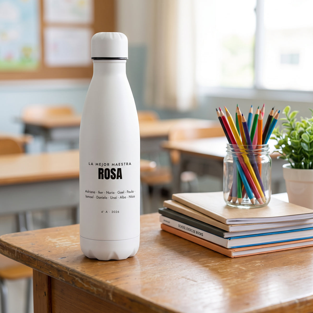 La botella de la maestra ROSA sobre la mesa del aula, con lápices y libros