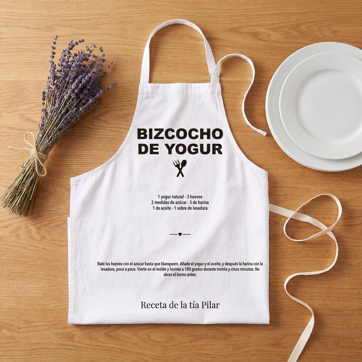 Delantal personalizado con la receta del bizcocho de yogur de la tía Pilar, doblado sobre una mesa de roble con lavanda y una cinta, listo para regalar