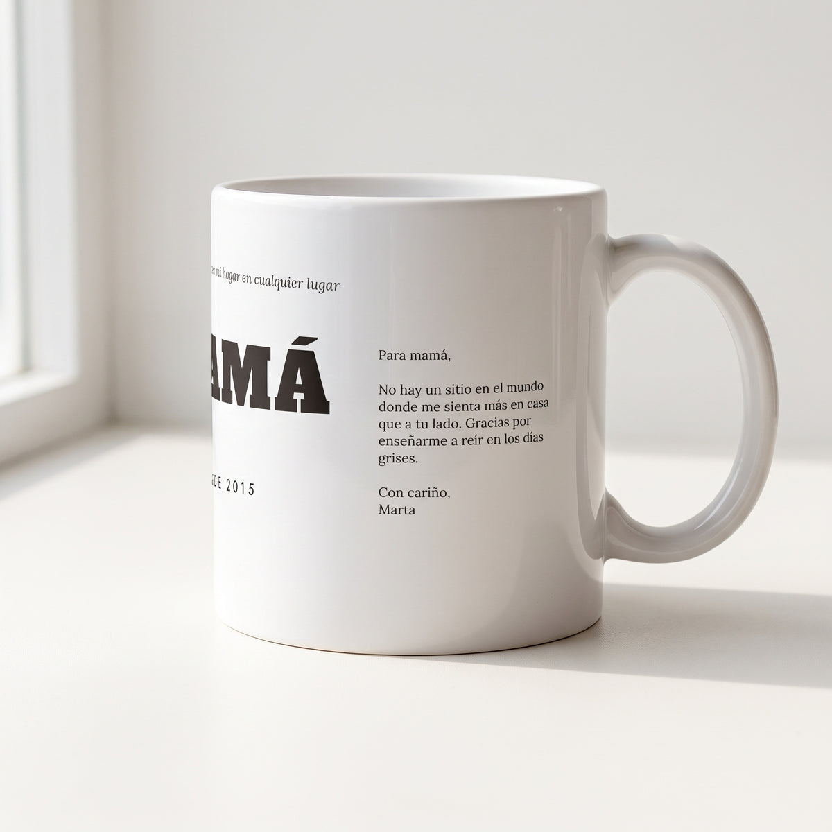 Taza MAMÁ con dedicatoria (Mamá, gracias por ser mi hogar en cualquier lugar · MAMÁ · DESDE 2015): la misma taza girada: la carta impresa en el costado, junto al asa