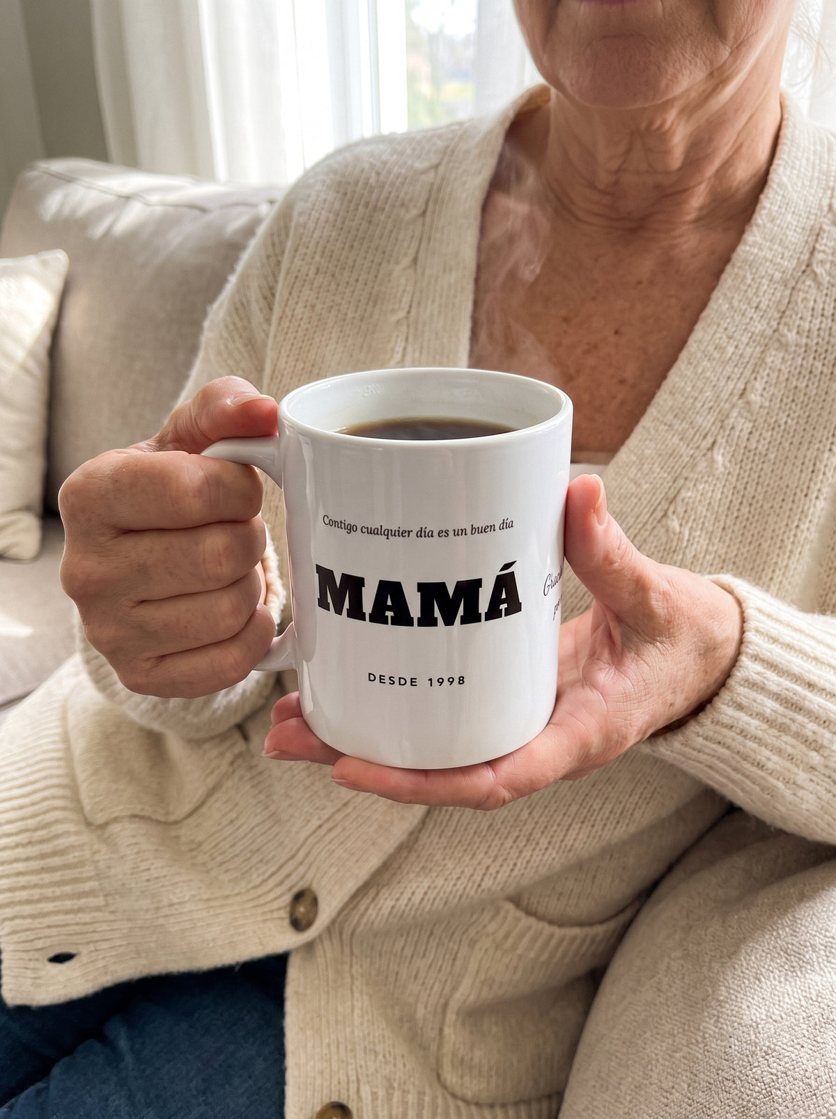 Taza MAMÁ con dedicatoria (Contigo cualquier día es un buen día · MAMÁ · DESDE 1998 · Gracias por todo): entre las manos, con café caliente