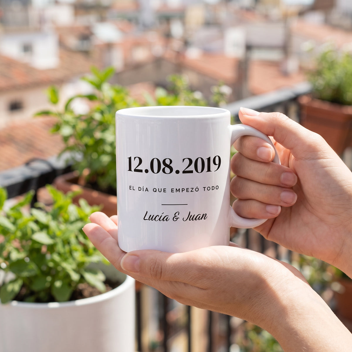 Manos sujetando la taza de pareja con la fecha en un balcón al sol