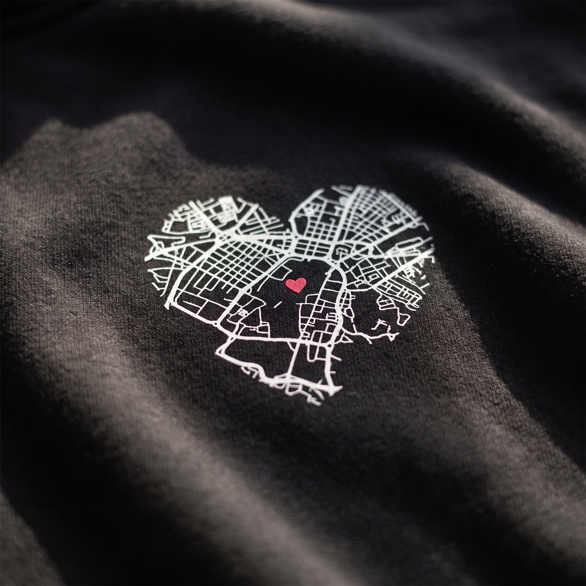 Detalle del estampado DTF de tres mapas en corazón: Salamanca, Toledo y Madrid sobre el tejido de una sudadera con capucha negra